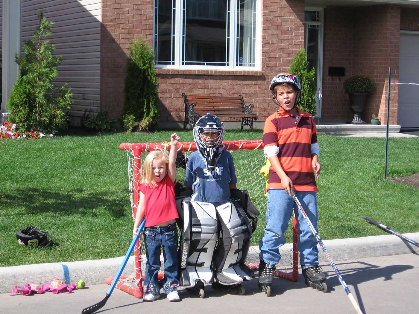 three young children are posed in front of a street hockey goal