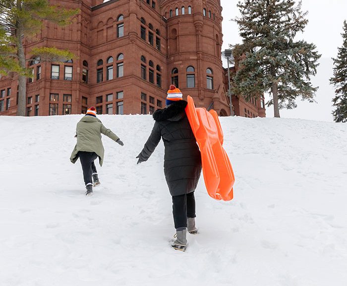 students walking up to crouse to slide down the snow covered hill