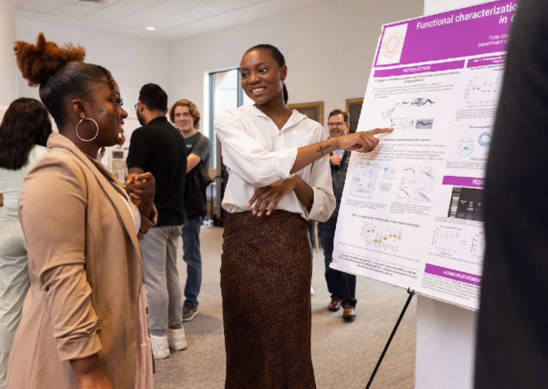 A women points to a research poster while talking with another women.