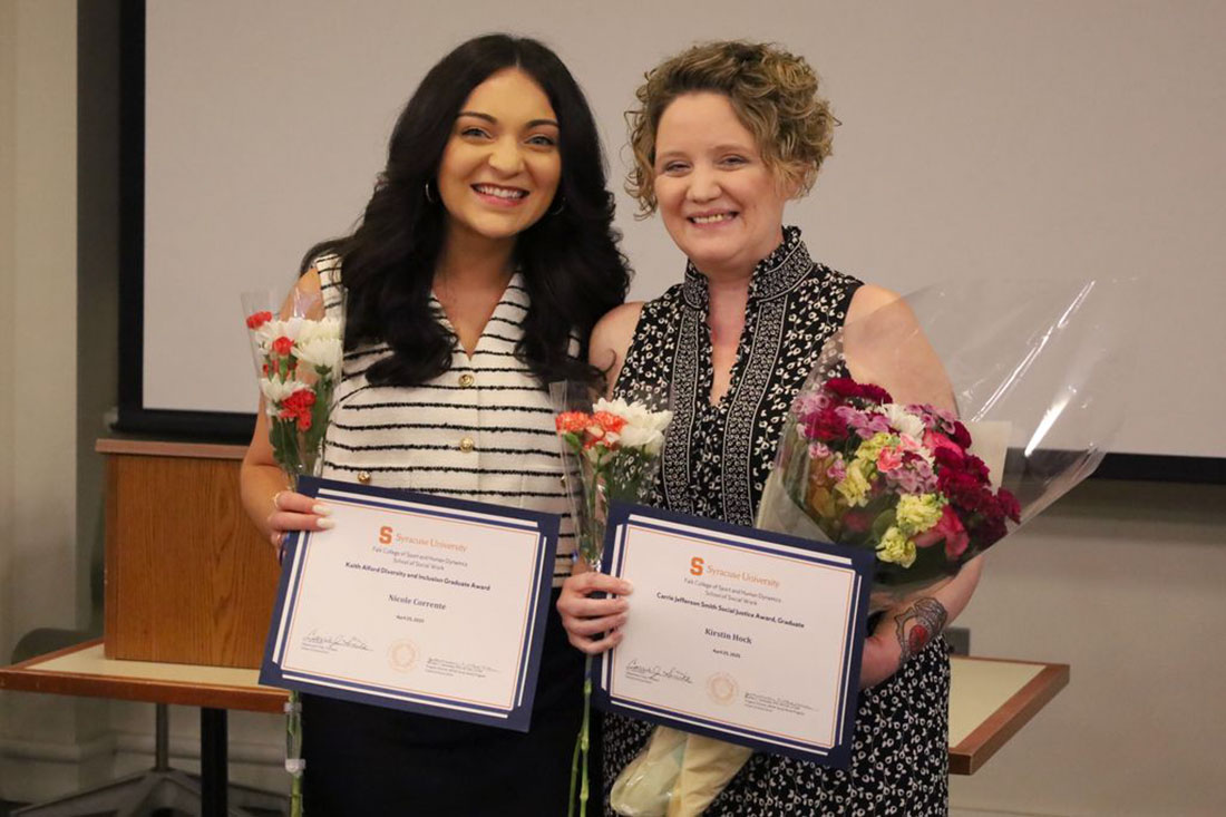 Two women holding awards, on left woman has long dark hair and a black and white striped blouse. Woman on the right has short blonde hair and is wearing a black and white floral shirt. Both women are holding certificates and flowers