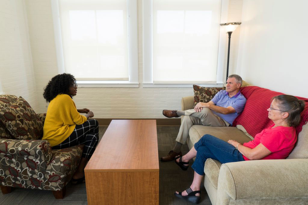 one man and one woman sitting on a couch across from a young woman sitting in a chair