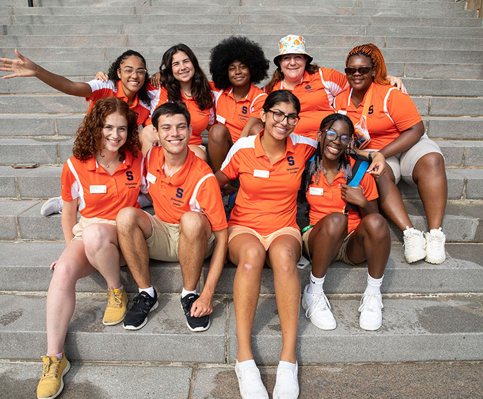 9 students sitting on steps on campus campus welcoming new students